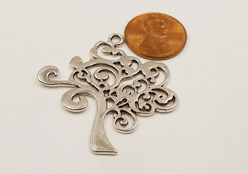 May include: Silver filigree tree charm with a decorative design. The charm is about the size of a UK penny.