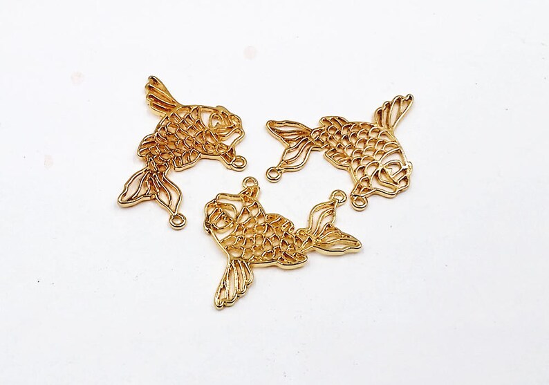 May include: Three gold-colored metal fish charms with intricate cut-out designs. The charms are perfect for jewelry making, scrapbooking, and other craft projects.