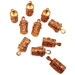 May include: A collection of ten gold-toned metal charms, each featuring an intricate, ornate design. The charms are shaped like small, cylindrical boxes with lids, and they have a loop at the top for attaching to a necklace or bracelet.