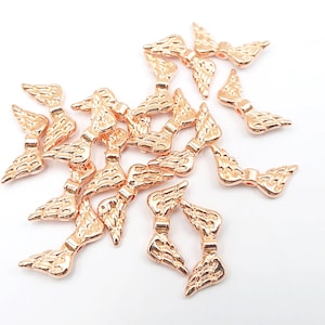 May include: A group of 18 rose gold angel wing charms. The charms are small and delicate, with a slightly textured finish. They are perfect for adding a touch of elegance to jewelry or crafts.