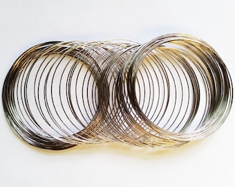 May include: A bundle of silver-colored wire rings, stacked and overlapping. The rings are thin and flexible, and they are all the same size.