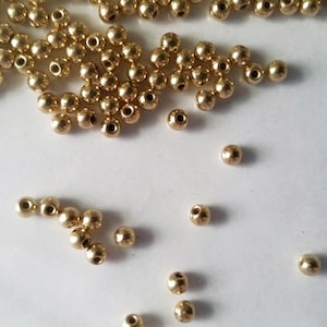 May include: A large pile of gold-colored round beads, with a few scattered on a white surface.