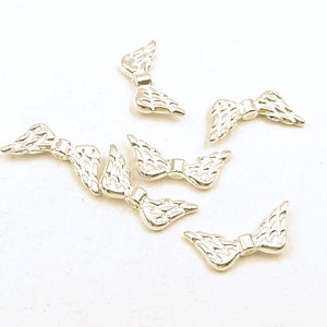 May include: Six silver angel wing charms, each with a delicate, detailed design. The wings are slightly curved and have a slightly textured surface.