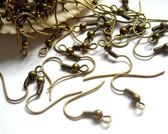 May include: A pile of gold-toned earring hooks with a spring and a small ball at the top. The hooks are scattered on a white surface.