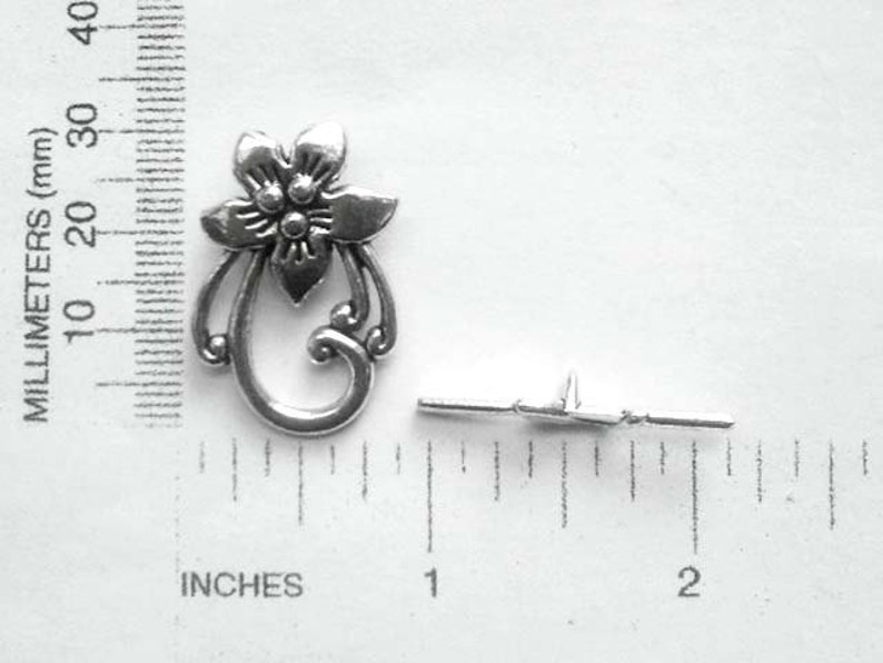 May include: Silver-toned metal flower charm with a decorative swirl design. The charm is approximately 1 inch in length and includes a jump ring for attaching to jewelry or other crafts.