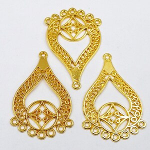 May include: Three gold filigree teardrop-shaped metal charms with a decorative circle in the center and five jump rings at the bottom.