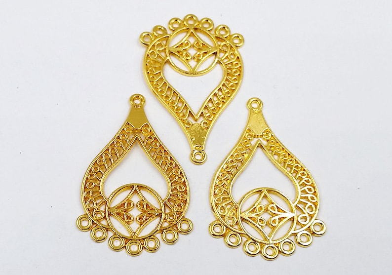 May include: Three gold filigree teardrop-shaped metal charms with a decorative circle in the center and five jump rings at the bottom.