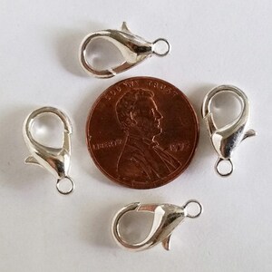 May include: Four silver-toned lobster claw clasps, each with a small loop, are arranged around a US penny. The penny is dated 1995 and has the inscription "In God We Trust" and "Liberty".