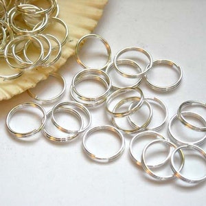 May include: A pile of silver jump rings, a type of jewelry finding, scattered on a white surface. The rings are small and circular, with a smooth, shiny finish.
