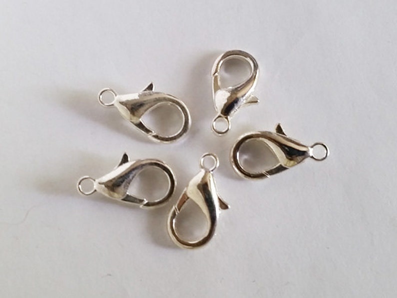 May include: Five silver lobster claw clasps, a type of jewelry finding used for attaching chains or cords to jewelry pieces.