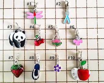 May include: A collection of ten small, decorative charms with silver-colored clasps. The charms feature various designs, including a dragonfly, ribbon, panda, cherries, a dress, a flower, a strawberry, a sandal, a purple flower, and a cherry.