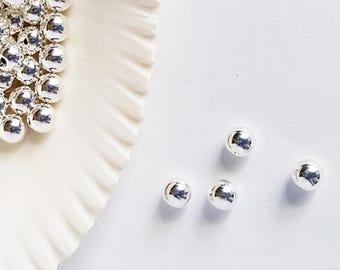 May include: Four silver metal beads on a white surface. The beads are round and shiny.