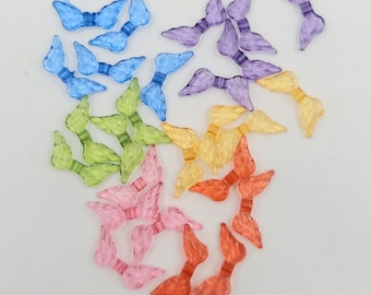 May include: Assortment of colorful plastic angel wings in various shades of blue, purple, green, yellow, pink, and orange. The wings are arranged in a circular pattern on a white background.