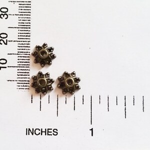 May include: Three antique gold-toned metal star-shaped beads with a hole in the center. The beads are approximately 1/2 inch in diameter.
