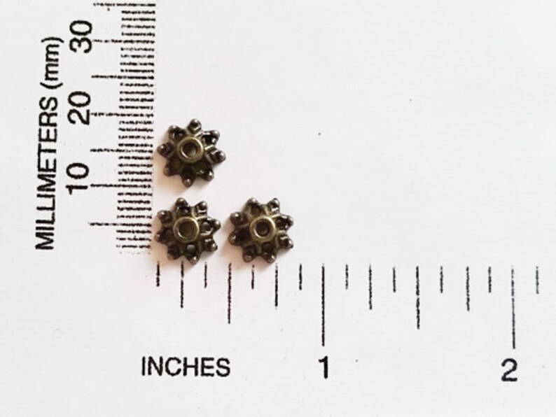 May include: Three antique gold-toned metal star-shaped beads with a hole in the center. The beads are approximately 1/2 inch in diameter.