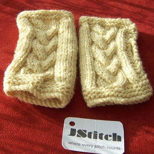 May include: A pair of cream-colored knitted wrist warmers with a cable knit pattern. The wrist warmers are on a red surface with a white tag that reads "jStitch where every stitch counts".