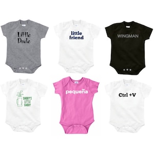 May include: Six different baby onesies with various designs and colors. The onesies feature the text "Little Dude", "little friend", "WINGMAN", "Daddy's Little Caddy", "pequeña", and "Ctrl + V".