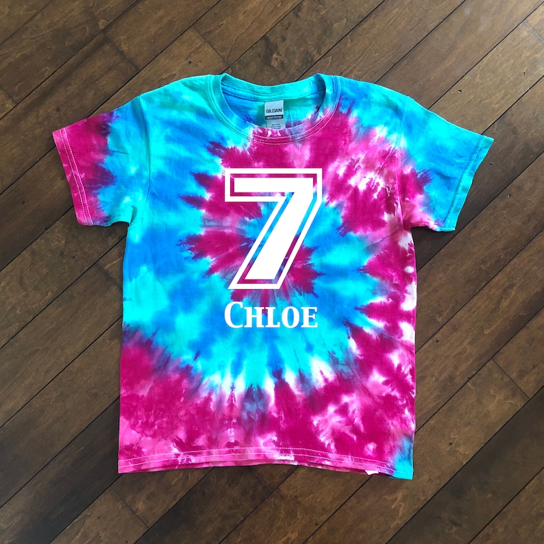 Pode incluir: Uma camiseta tie-dye em tons de azul e magenta. O n&uacute;mero 7 &eacute; impresso em branco com uma borda branca, e o nome "CHLOE" &eacute; impresso abaixo. A camiseta tem gola redonda e mangas curtas.
