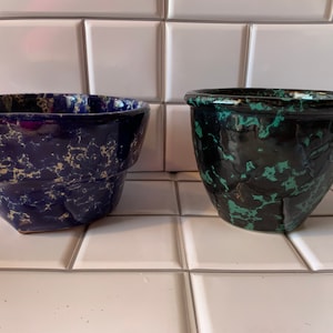 May include: Two ceramic planters, one blue with white speckles and one black with green speckles.