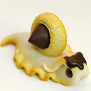 Könnte beinhalten: Eine fantasievolle, handgefertigte Schneckenfigur mit einer Schokoladenschale und einem weißen Körper mit Schokoladenüberzug. Die Schnecke hat ein einzelnes, weißes Horn.
