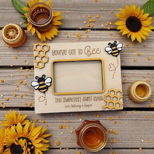 May include: Wooden picture frame with the text "you've got to Bee" and "The Sweetest Aunt Ever". The frame has bee and honeycomb accents, with sunflowers and honey jars scattered around.