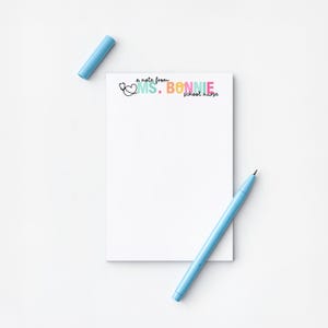May include: A white notepad with the text "a note from MS. BONNIE school nurse" in colorful lettering. A light blue pen and pen cap are also in the image.
