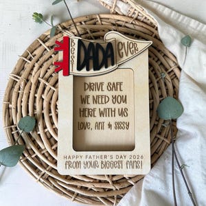 May include: A wooden picture frame with the words "Best Dada Ever" in black and red. The frame includes the text "Drive safe, we need you here with us, love, Ant & Sissy" and "Happy Father's Day 2026 from your biggest fans!"