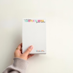 May include: A white notepad with the text "a note from HARPER'S MOM gina carter" in colorful lettering. The notepad is held by a person's hand, and the bottom of the notepad has a phone number and email address.