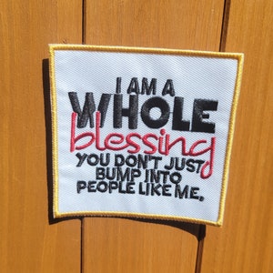 May include: A white embroidered patch with a yellow border. The text reads "I am a whole blessing you don't just bump into people like me."
