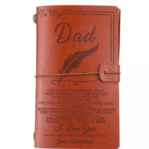 May include: A brown leather journal with the words "To My Dad" embossed on the cover, along with a feather design. The journal includes a quote from a daughter to her father. A leather strap secures the journal.