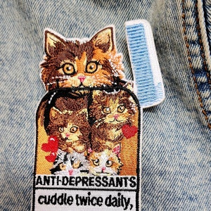 May include: Embroidered iron-on patch with a cartoon image of a stack of cats with hearts and the text "Anti-depressants cuddle twice daily, repeat as necessary".