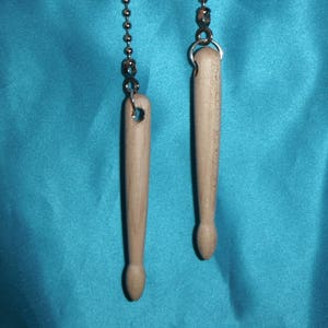 May include: Two wooden dowel rods with silver chain and metal rings hanging from them. The dowel rods are suspended against a bright turquoise background.
