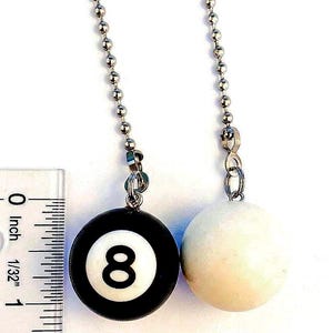May include: Two ceiling fan pull chains. One features a black and white 8-ball design, the other a white ball. Both hang from a silver ball chain. A ruler shows the 8-ball is about 1 inch in diameter.