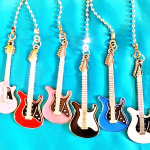 May include: Six miniature electric guitars in different colors, including pink, red, black, blue, and white, hanging from silver chains. The guitars are all in the same style, with a single pickup and a tremolo bar.