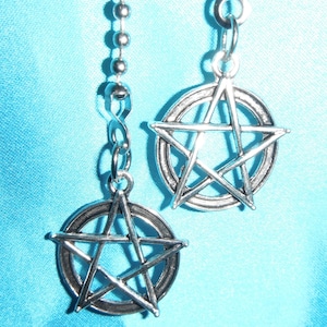 May include: Two silver pendant earrings with a pentagram design. Each earring features a five-pointed star inside a circle, hanging from a silver chain.