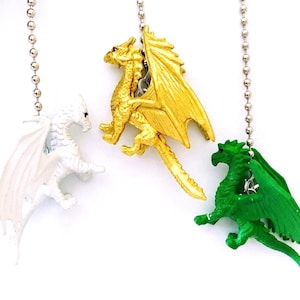 May include: Three dragon-shaped ceiling fan pulls in white, gold, and green. Each dragon is suspended from a silver ball chain. The dragons have detailed wings and are posed in a dynamic stance against a white background.