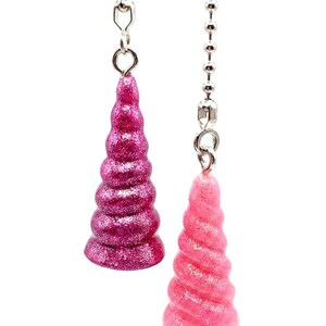 May include: Two glittery unicorn horn-shaped ceiling fan pulls. One is a deep pink, the other a lighter pink. Both are attached to silver ball chains.
