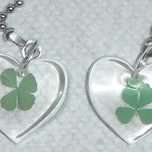 May include: Two clear heart-shaped pendants with silver chains. Each pendant contains a pressed four-leaf clover.