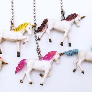 May include: A collection of white unicorn figurines with colorful manes and tails, including red, yellow, pink, and blue. Each unicorn is attached to a silver chain, suggesting they are decorative items.