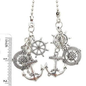 May include: Silver-toned nautical-themed earrings. Each earring features a compass, ship's wheel, anchor, and a smaller wheel charm. The earrings are approximately 2 inches in length.