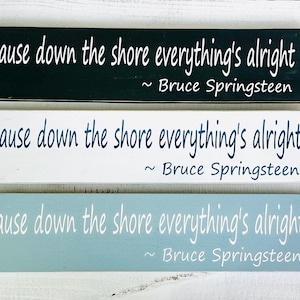 May include: Three wooden signs with the same text: 'cause down the shore everything's alright ~ Bruce Springsteen. The signs are black, white, and light blue.