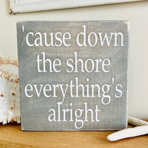 May include: A gray wooden sign with white text that reads 'cause down the shore everything's alright'.