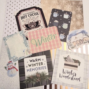 May include: A collection of winter-themed paper cutouts and stickers. Includes cards with text like "Hot Cocoa," "Winter," and "Winter Wonderland." Features images of snowmen, mugs, and winter scenes. Various patterns and colors.