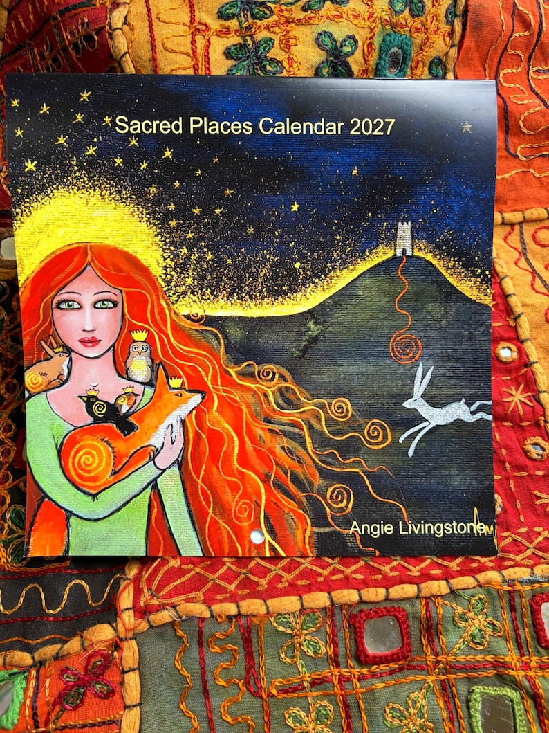 Puede incluir: Un calendario de pared cuadrado titulado Sacred Places Calendar 2027 de Angie Livingstone. La portada presenta una pintura de una persona con cabello largo y rojo sosteniendo un zorro, un b&uacute;ho y dos p&aacute;jaros. Una liebre blanca corre por un paisaje oscuro.