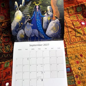 Puede incluir: Un calendario de pared para septiembre de 2027 con una ilustraci&oacute;n de una figura con astas, un lobo y p&aacute;jaros entre piedras erguidas bajo un cielo iluminado por la luna. La cuadr&iacute;cula muestra el mes, los d&iacute;as y las fases lunares.