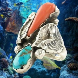 May include: A silver ring featuring a large, teardrop-shaped coral stone and a turquoise stone. The ring has intricate leaf-like designs and a polished finish. The coral is a vibrant orange, and the turquoise has brown matrix.