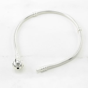 A silver bracelet with a round charm is shown on a white marble surface.