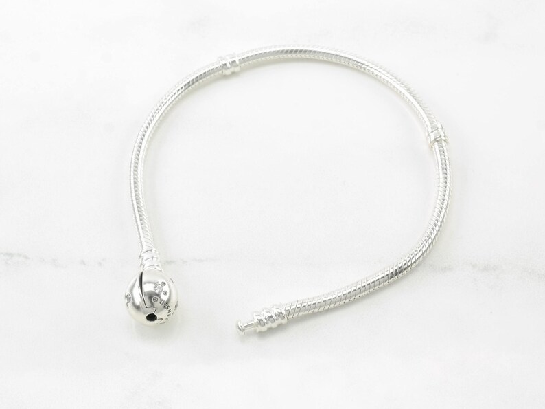 A silver bracelet with a round charm is shown on a white marble surface.