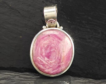 May include: Oval pendant with a pink stone, featuring a swirl pattern, set in a silver-coloured metal frame. The pendant has a silver bail with a spiral design and small decorative accents.
