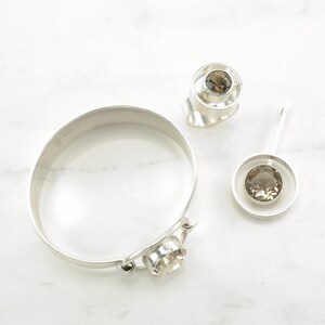 Peut inclure: Un ensemble de trois bijoux en argent avec des pierres pr&eacute;cieuses brunes. L'ensemble comprend une bague, un bracelet et un pendentif. La bague et le pendentif pr&eacute;sentent un design circulaire avec une pierre pr&eacute;cieuse au centre. Le bracelet est une simple bande avec une pierre pr&eacute;cieuse attach&eacute;e au fermoir.
